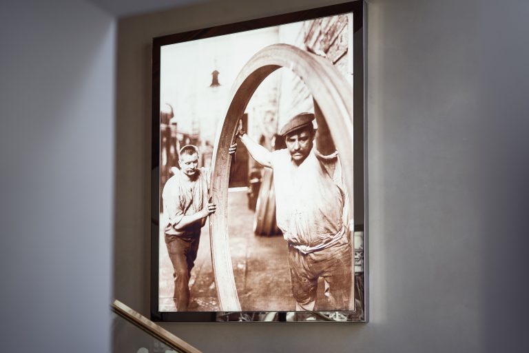 Framed historical photograph of two people carrying a large metal ring.