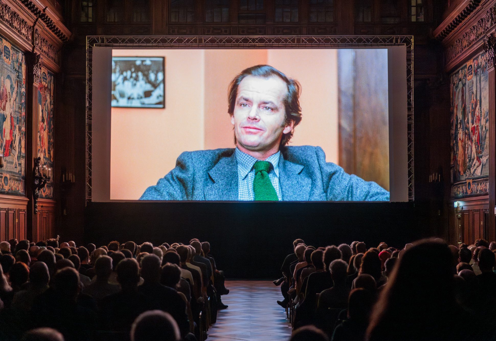 Das Publikum sitzt vor der Leinwand. Zu sehen ist ein Filmstill von Jack Nicholson