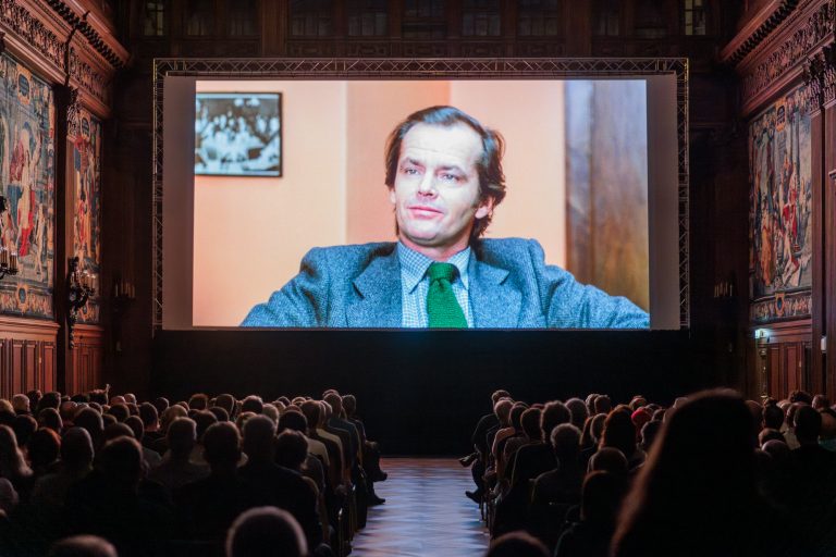 Das Publikum sitzt vor der Leinwand. Zu sehen ist ein Filmstill von Jack Nicholson