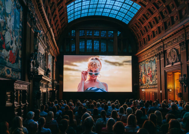 Das Publikum sitzt vor der Leinwand und sieht den Film "Barbie" in der Oberen Halle