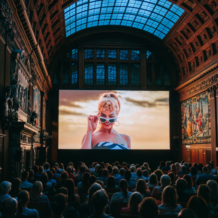Das Publikum sitzt vor der Leinwand und sieht den Film "Barbie" in der Oberen Halle