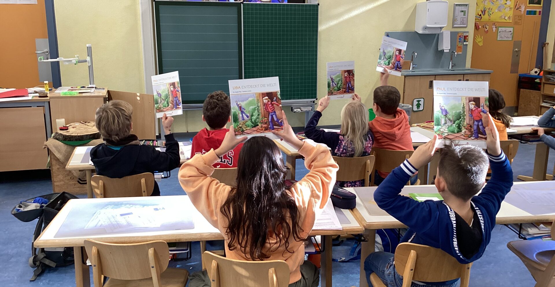 Schüler*innen einer Grundschulklasse sitzen mit dem Rücken zum Fotografen und halten Bücher hoch.
