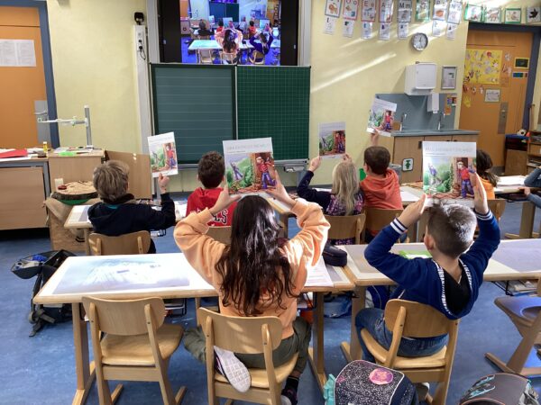 Schüler*innen einer Grundschulklasse sitzen mit dem Rücken zum Fotografen und halten Bücher hoch.