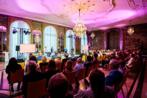 Blick in den Gartensaal, in dem fünf Personen auf der Bühne sitzen vor einem Publikum