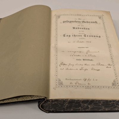 Eine aufgeschlagene Bibel liegt auf einem Tisch. Auf der erste Seite ist zu lesen: "In gesegnetem Gebrauch und zum Andenken an den Tag Ihrer Trauung den 15. Oktober 1906 erhielten von dem Priester aus Werden a.d. Ruhr dieses Bibelbuch: Gustav Georg Friedrich Maria Krupp von Bohlen und Halbach und Bertha Krupp."