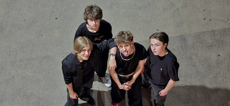 Die vier Bandmitglieder von Pure Panic stehen nebeneinander, tragen schwarze Kleidung und schauen nach oben in die Kamera, die in Vogelperspektive positioniert ist.