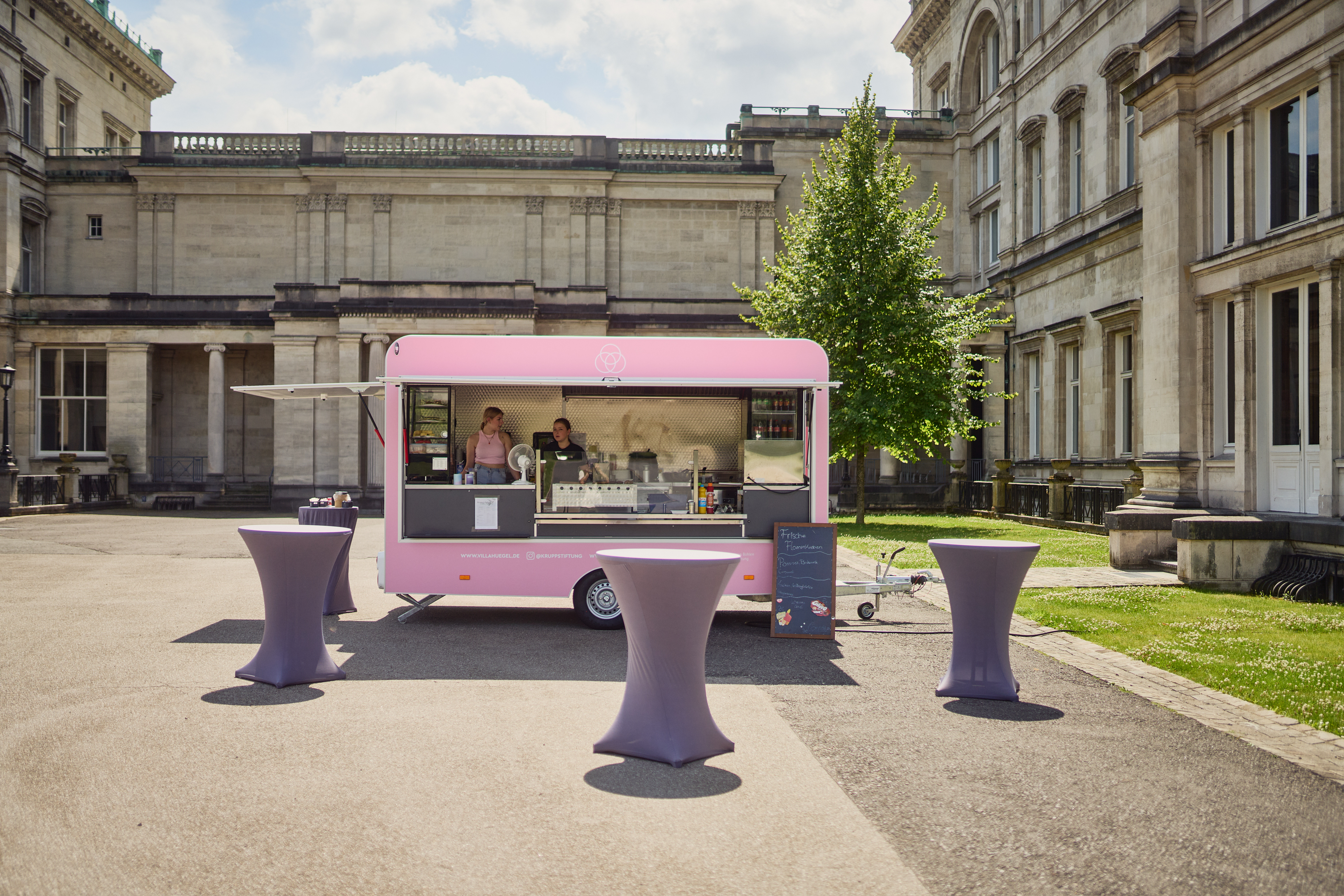 Ein rosafarbener Foodtruck mit Stehtischen vor der Villa Hügel.