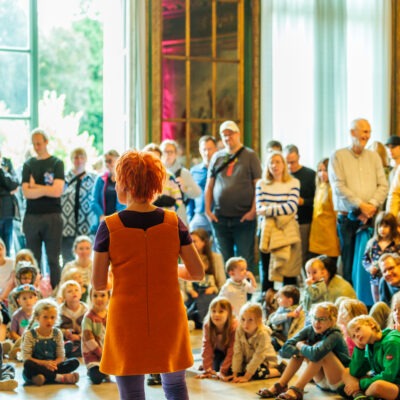 Viele Erwachsene und Kinder, die im Halbkreis sitzen und einer Person zuschauen.