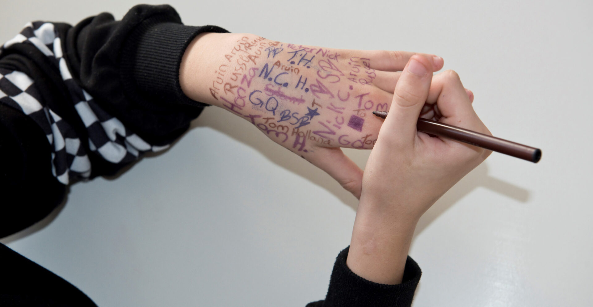Ein paar Hände: Die rechte Hand schreibt mit einem Stift auf die linke Hand, die bereits voll geschrieben ist.