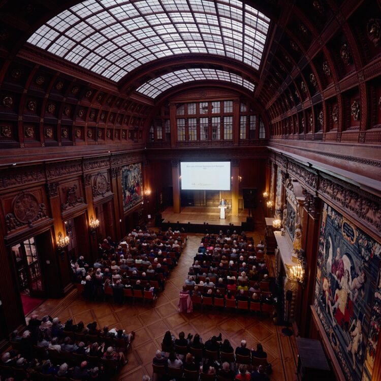 Vortragsveranstaltung in der Oberen Halle mit einem Redner am Pult vor einer Leinwand und Personen im Publikum.