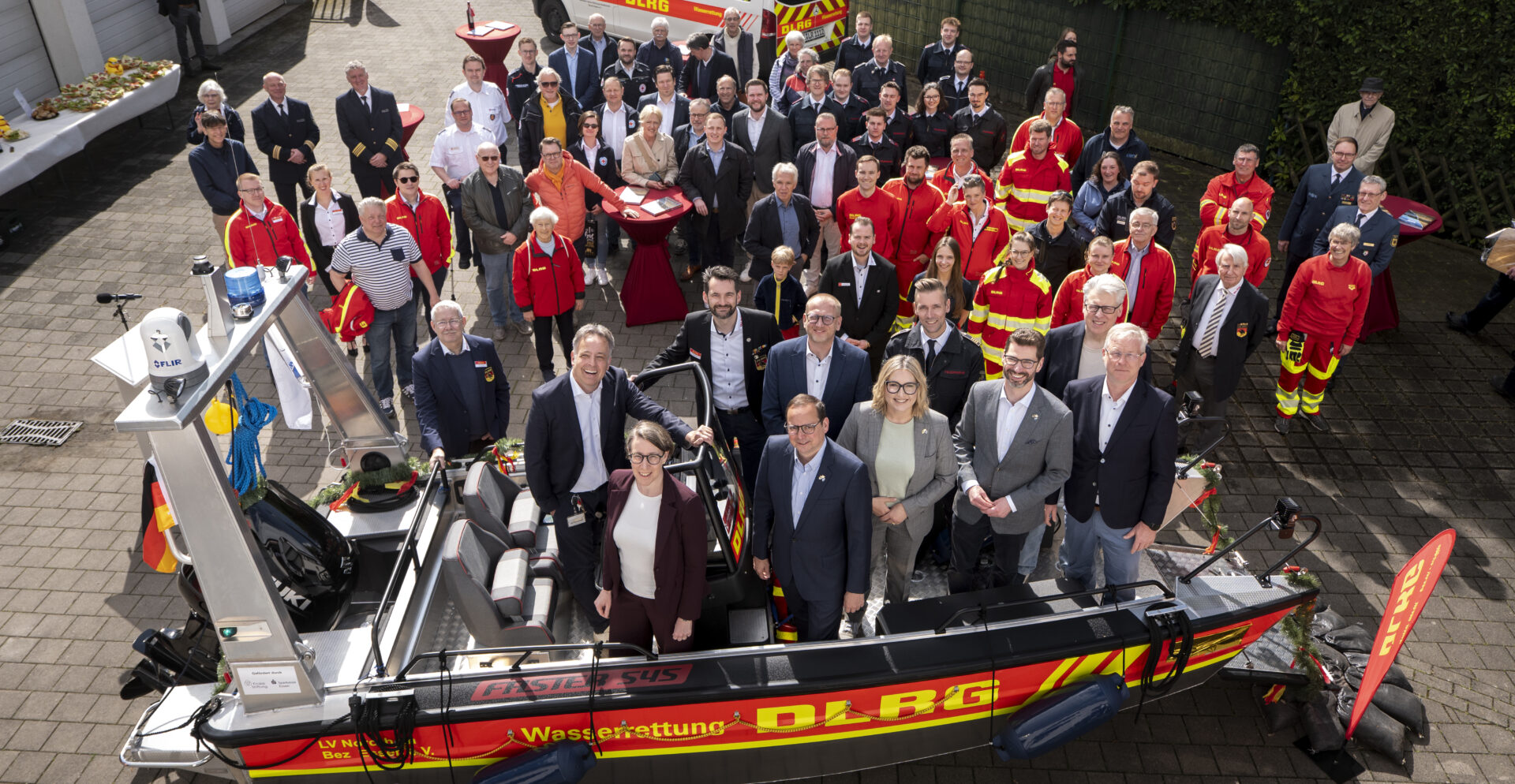 Menschen die in einem DLRG Rettungsboot stehen und um das Boot herum, von oben fotografiert.