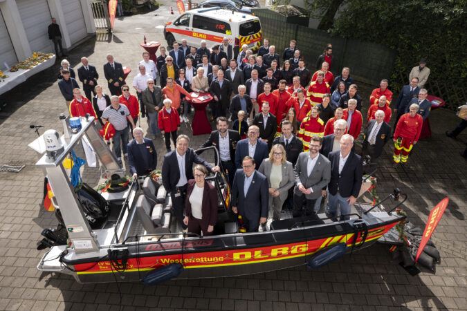 Menschen die in einem DLRG Rettungsboot stehen und um das Boot herum, von oben fotografiert.