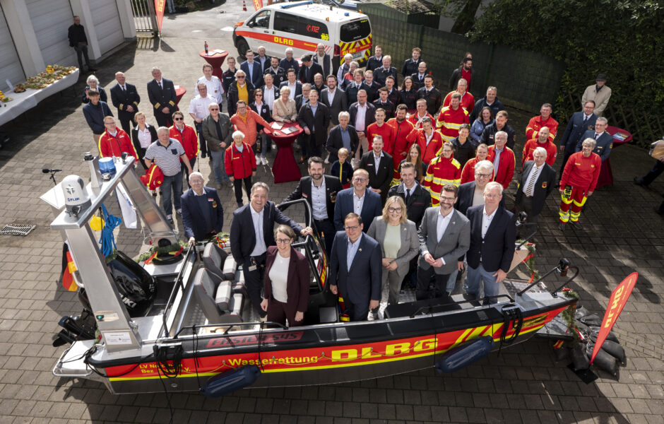 Menschen die in einem DLRG Rettungsboot stehen und um das Boot herum, von oben fotografiert.