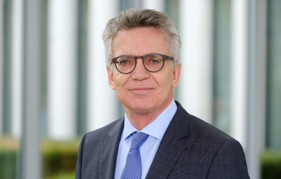 Dr. Thomas de Maizière, im dunklen Anzug mit blauer Krawatte als Portrait vor unscharfem Hintergrund.