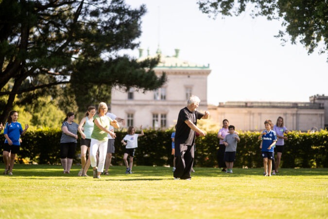 Eine Gruppe von Kindern und Erwachsenen bei Tai Chi im Hügel-Park.