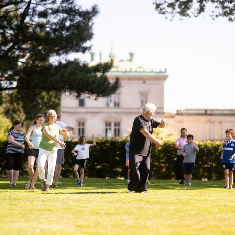 Eine Gruppe von Kindern und Erwachsenen bei Tai Chi im Hügel-Park.