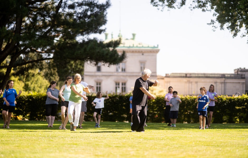 Eine Gruppe von Kindern und Erwachsenen bei Tai Chi im Hügel-Park.