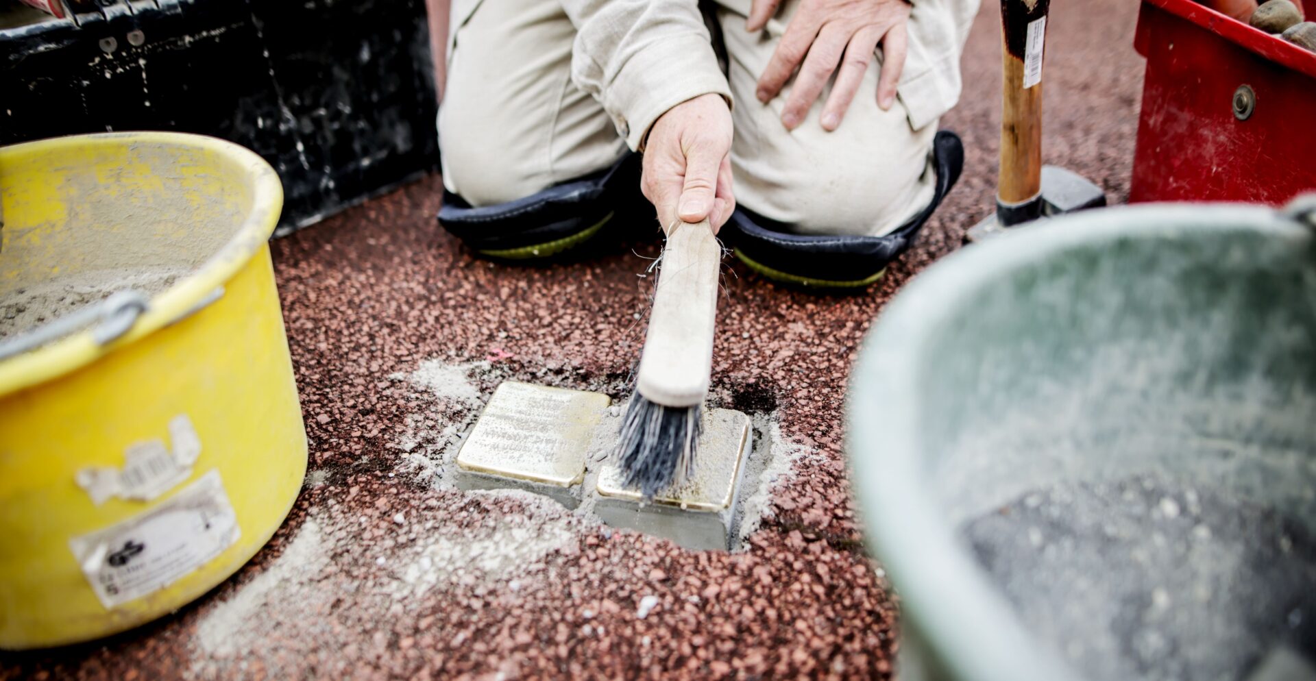 Neu gelegte Stolpersteine, die mit einem Handfeger gereinigt werden.