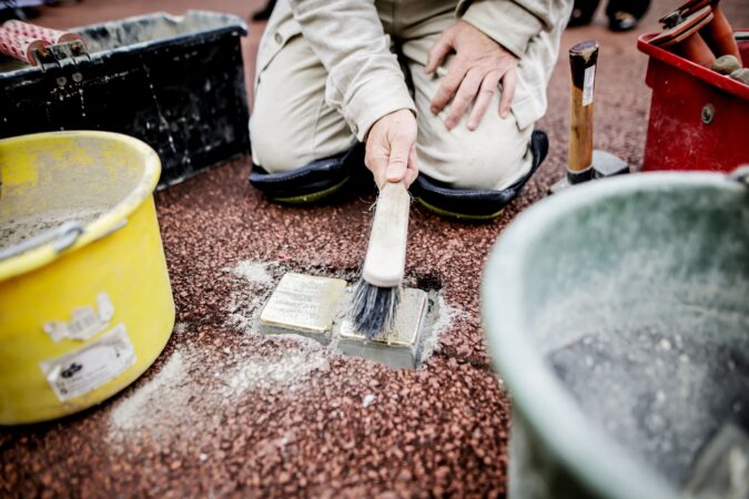 Neu gelegte Stolpersteine, die mit einem Handfeger gereinigt werden.