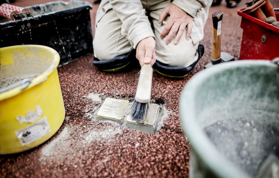 Neu gelegte Stolpersteine, die mit einem Handfeger gereinigt werden.