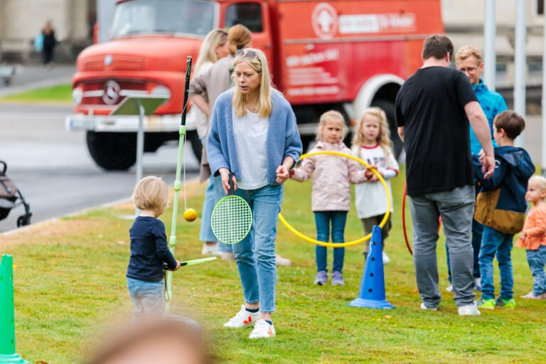 Im Hintergrund ist das Spielmobil zu sehen mit Kindern und Erwachsenen im Vordergrund