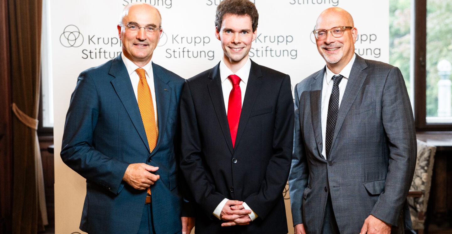 Three men in front of a press wall.